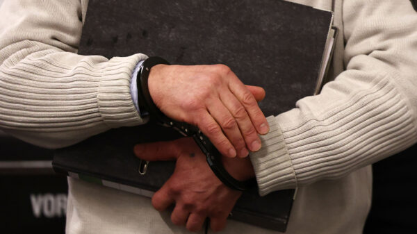 Person holding binder and is in handcuffs.