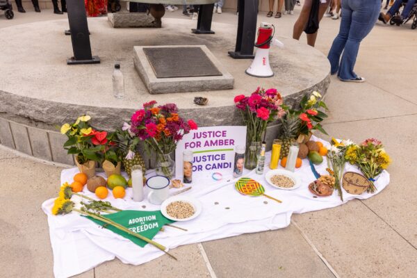 A memorial of flowers, candles, fruit, etc, and a sign that reads Justice for Amber and Justice for Candi.