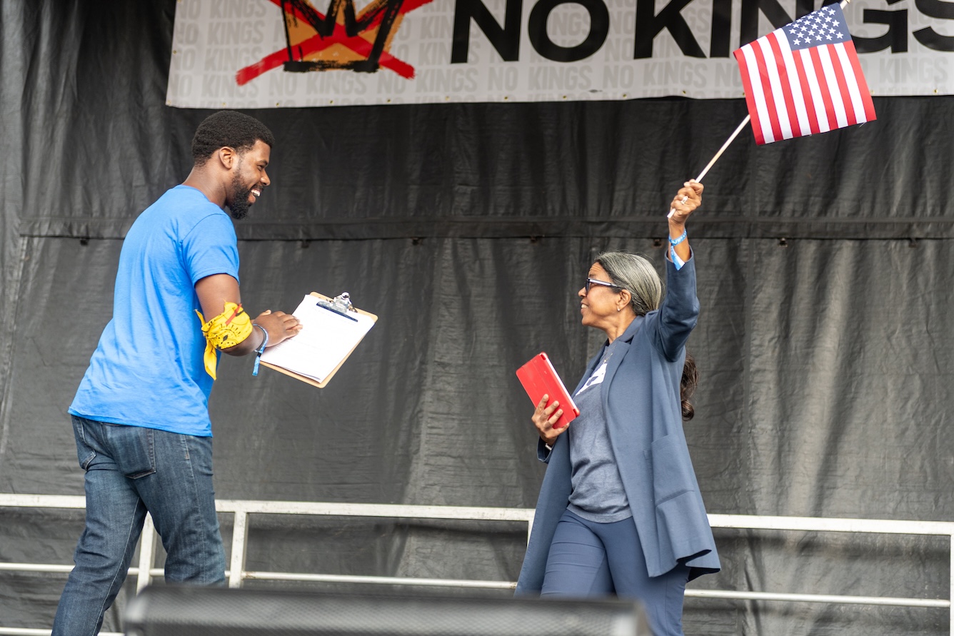 ACLU Policy and Advocacy Director Christopher Bruce joyously welcomes Executive Director Andrea Young to the stage while she waves an American flag at the October 18, 2025 No Kings rally.