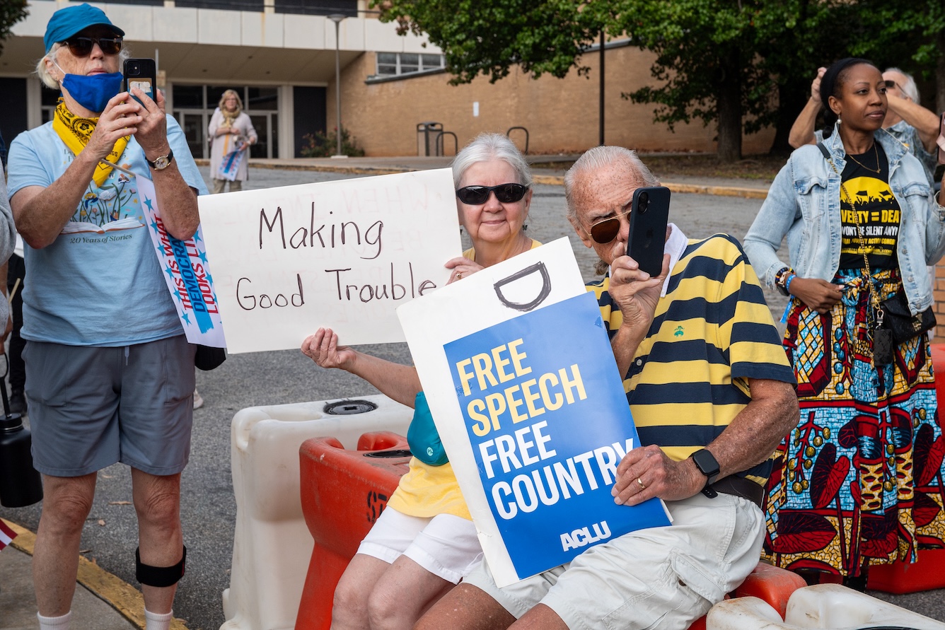 A man and a woman hold signs saying Making Good Trouble, and Free Speech Free County at the No Kings Rally on October 18, 2025.