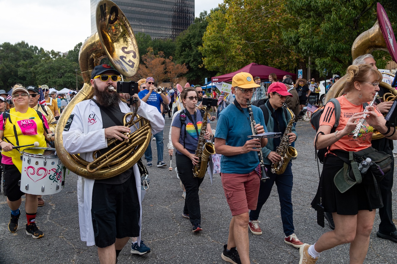 A band with members playing a tuba, flutes, saxophones, a drum and more during the October 18, 2025 No Kings Rally at the Atlanta Civic Center.