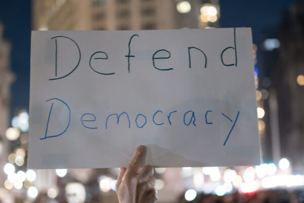 Protestor holding a sign that reads, "Defend Democracy."