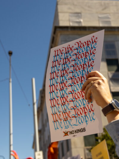 A hand risen among people at a protest, holding a sign reading "We the people."