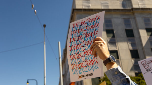 A hand risen among people at a protest, holding a sign reading "We the people."