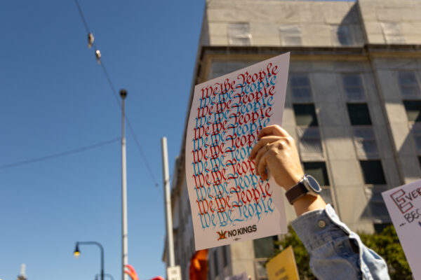 A hand risen among people at a protest, holding a sign reading "We the people."