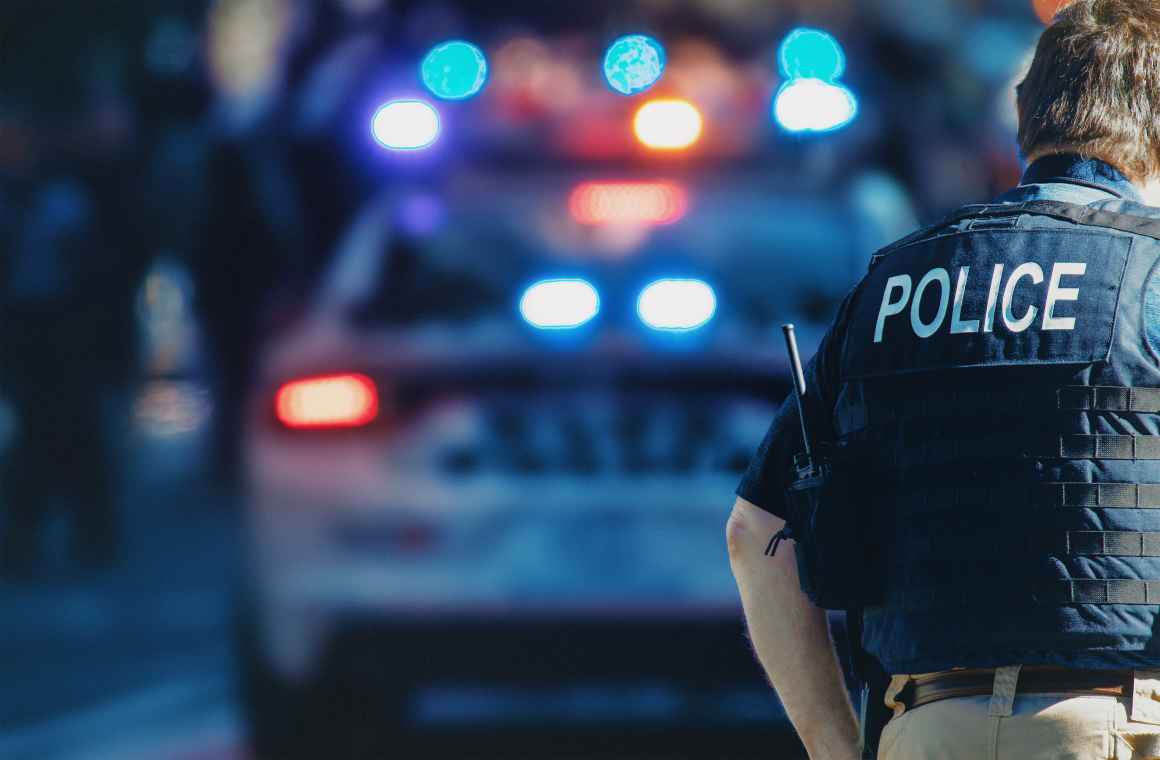Police officer in front of a police car with sirens on