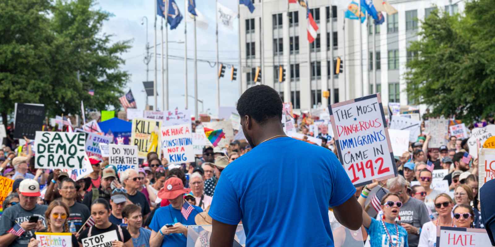 Policy Director Chris Bruce photographed from behind, standing in front of crowd at No Kings rally