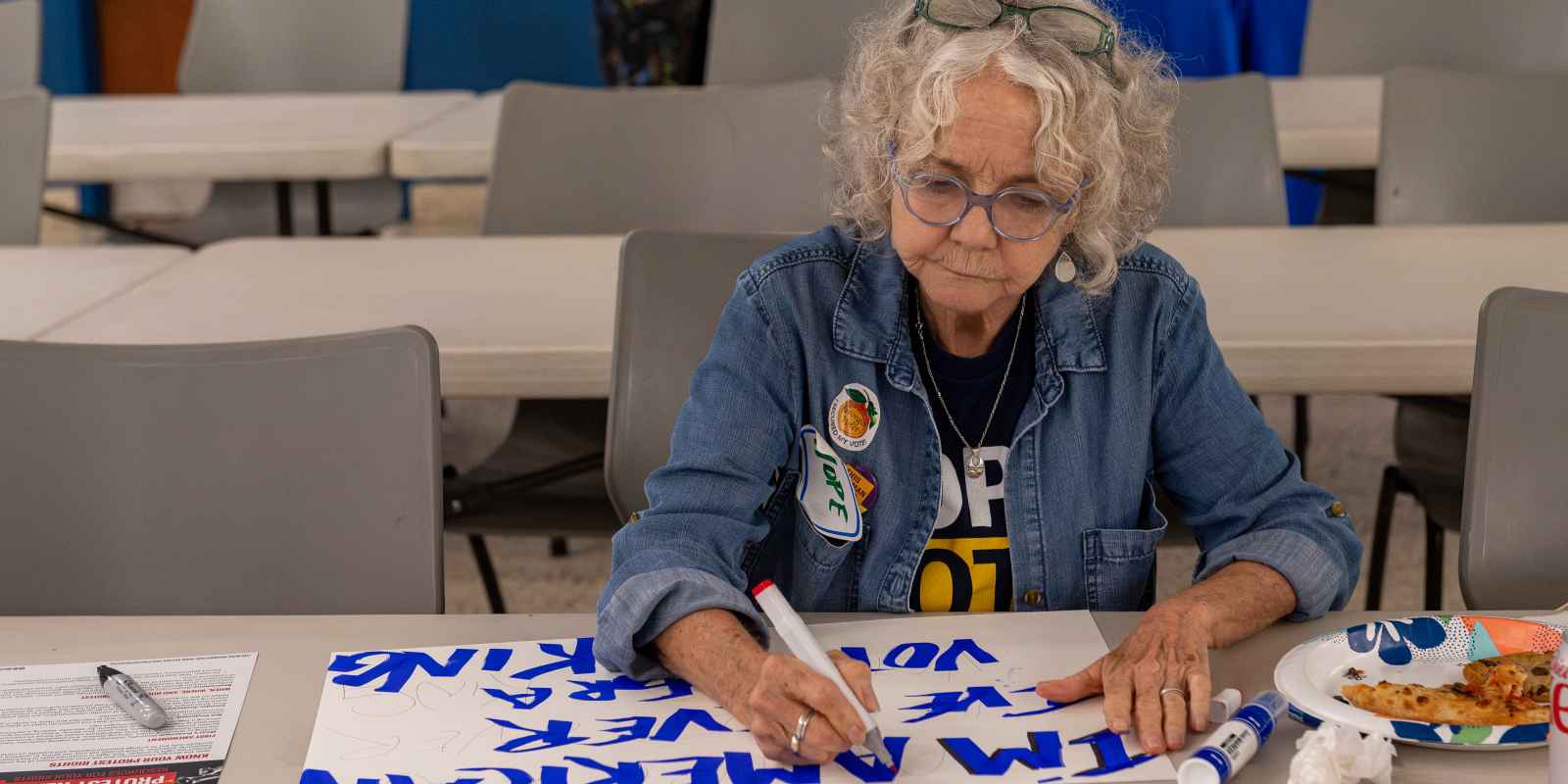 Woman making protest sign with markers, wearing jean jacket