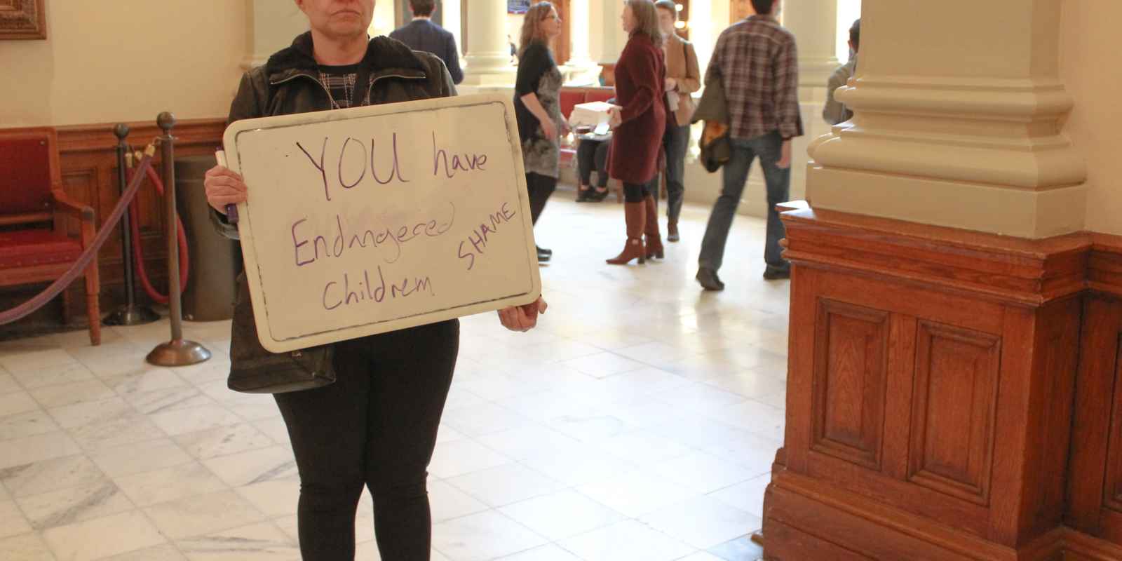 A parent stands with a handwritten sign outside of the Senate chambers following the passage of SB 140 on March 21, 2023