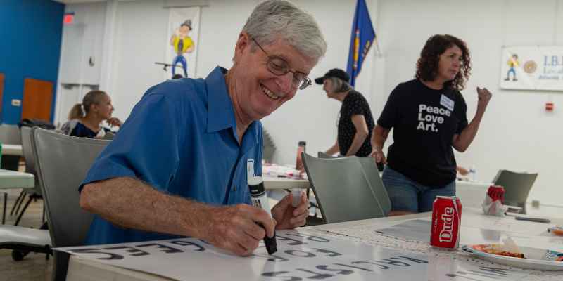 Man in blue shirt and glasses making protest sign