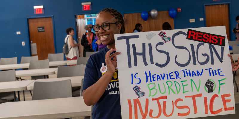 ACLU of Georgia volunteer holding sign that reads This Sign in Heavier than the burden of justice