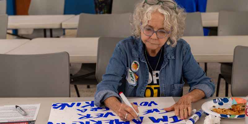 Woman making protest sign with markers, wearing jean jacket