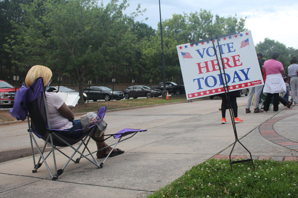 Person sitting in chair outside in front of "Vote Here Today" sign